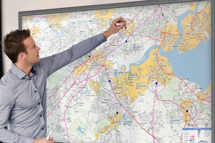 A man marking a framed regional wall map, its locations each ringed by a radius circle and labelled with a store number.