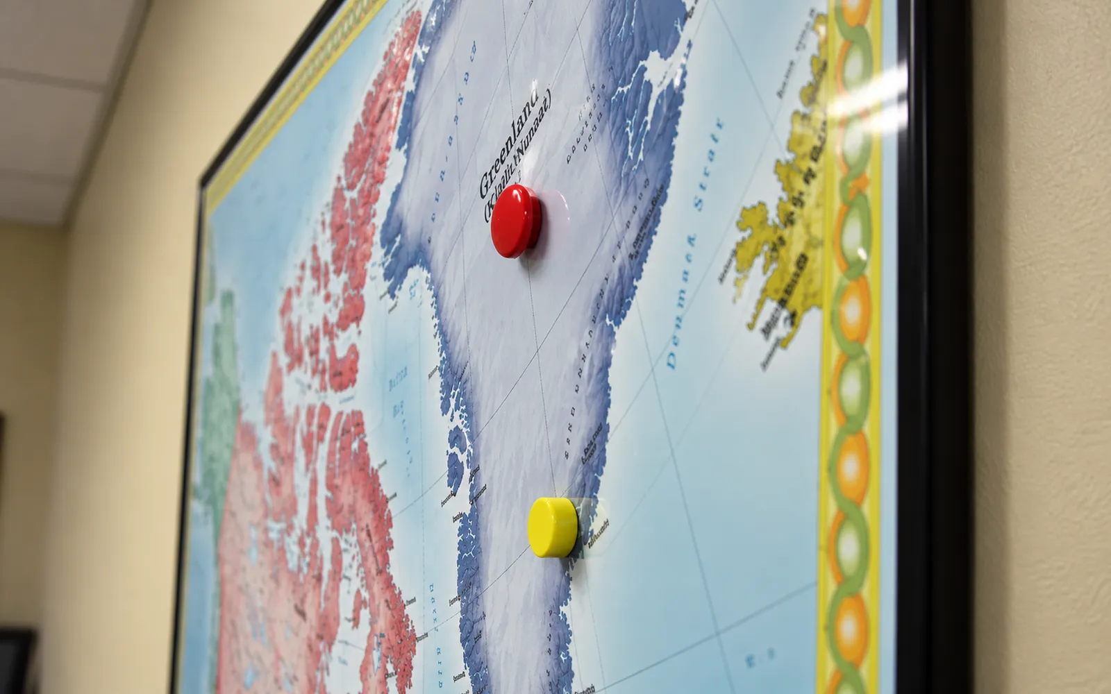 Red and yellow magnets stuck to Greenland on a black-framed wall map
