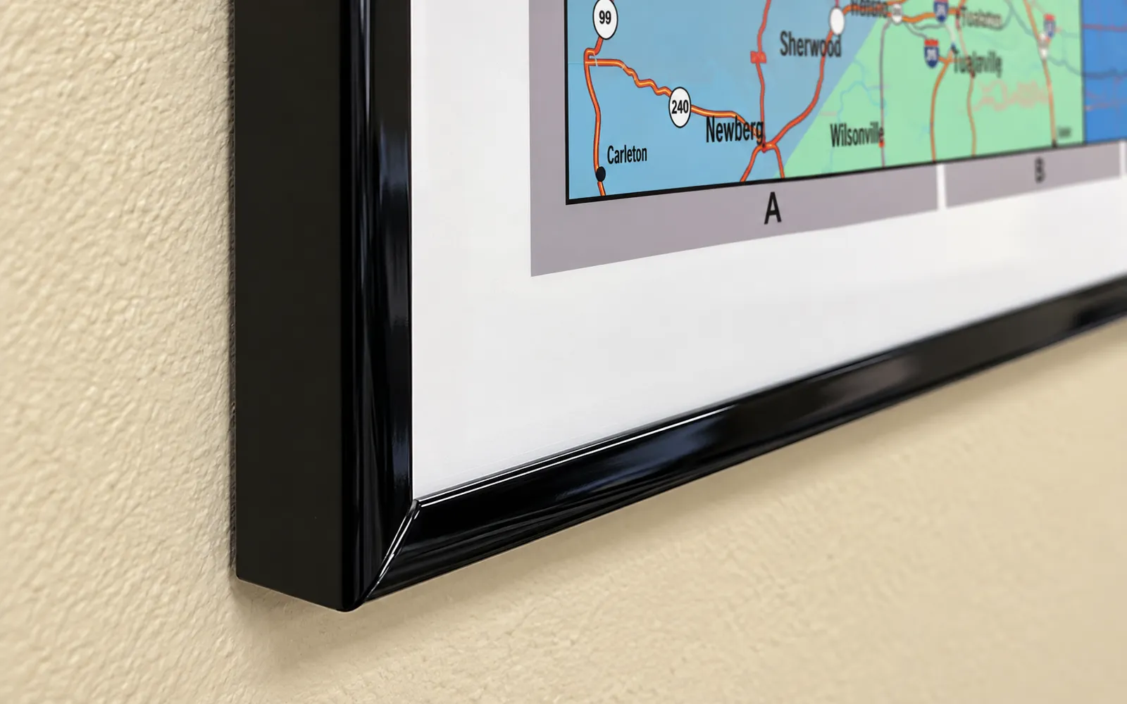 The glossy black corner of a plastic-framed map hung on a textured wall